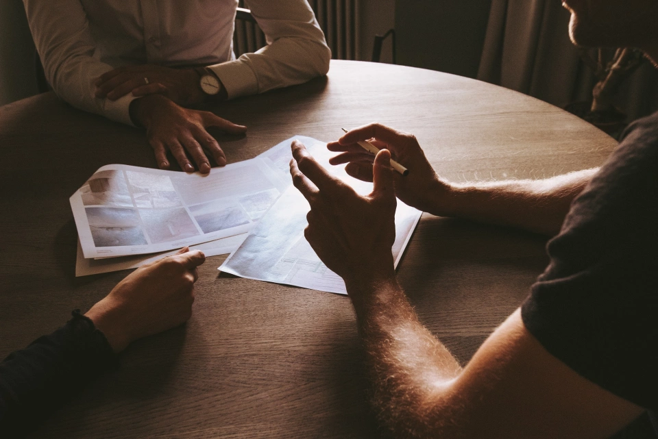 Three people sat around a round table. You can only see their hands and it looks like they are in deep conversation.