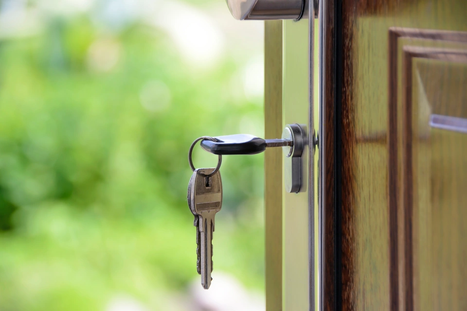 A zoomed in image of a set of keys in the lock of a door. The biggest key is in the lock while two other smaller keys hang off a keyring.